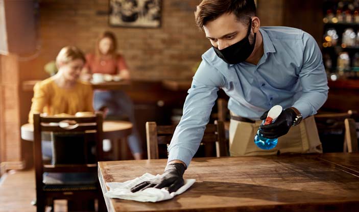 Photo: Drazen Zigic/shutterstock.com Bilde av servitør med munnbind som rengjør bord.